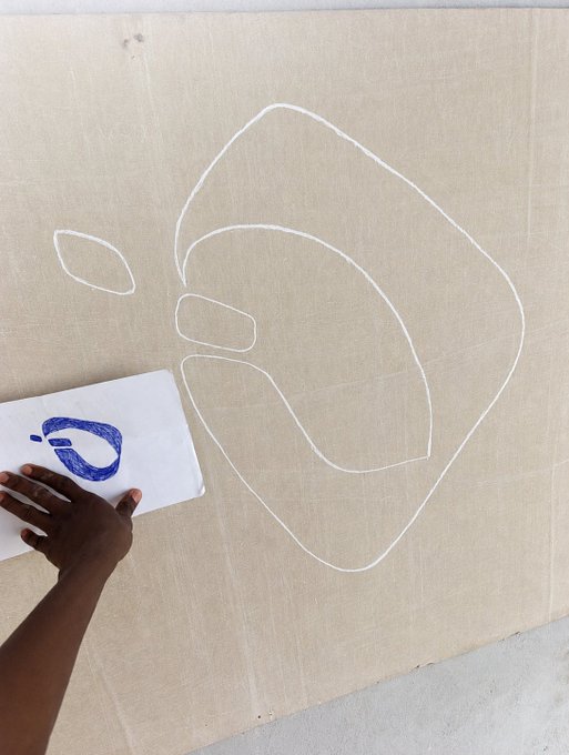 The image features a person's hand holding a piece of paper with blue lines drawn on it, which appears to be a sketch or drawing. The background of the image is a tan-colored wall, providing a neutral backdrop for the artwork. The caption above the image reads "Avec interlink lavenir de la Cryptomonnaie sera bien meilleur les petite entreprises peuvent facilement échanger leurs marchandises contre des ITL #InterLinkInMyLife #ITLG". This phrase is likely a reference to the artist's work or an artistic concept, possibly related to the image of the hand holding the paper with blue lines.