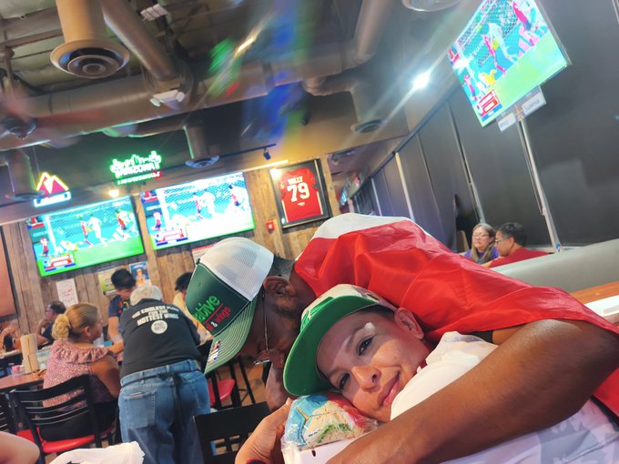 Two young men embrace at a sports bar with multiple TVs showing games in the background.