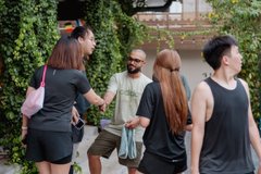 A group of people standing outdoors, with a man in the center wearing a face mask and sunglasses.