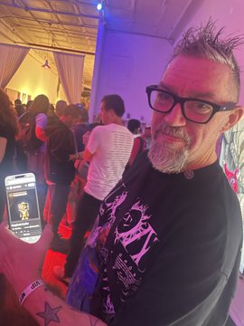 A bearded man with glasses takes a selfie at what appears to be the Canal Street Show in NYC, with another attendee visible in the background holding up a phone displaying an NFT minting screen, capturing the live crypto minting experience mentioned in the caption.