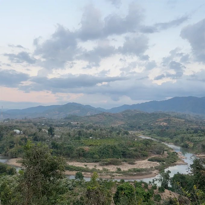 Scenic landscape view of a winding river through green hills and mountains under a cloudy sky at dusk.