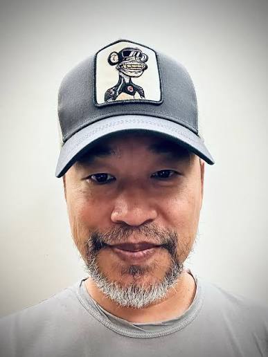 A man with a salt-and-pepper beard smiles while wearing a cap with an "8" logo patch, representing the trader known as Machi (@machibigbrother) who is featured in the post about his $8.44M weekly losses and his 9,950 ETH long position on hypurrscan.io.