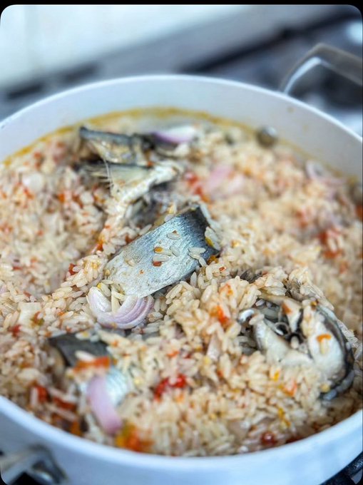 A large pot of rice cooked with sardines, tomatoes, and shallots sits on the stove—a hearty homemade meal that invites conversation and a shared moment of connection after a long day.