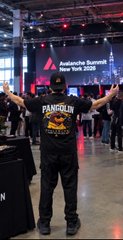 A person wearing a black "PANORAMA" shirt and cap stands with arms raised at the Avalanche Summit New York 2026 event.