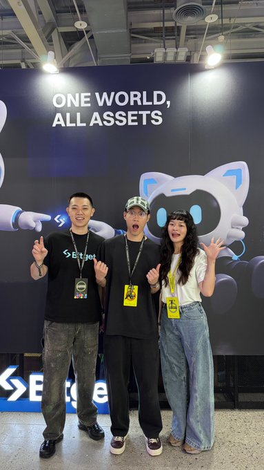 Three attendees pose cheerfully in front of a "ONE WORLD, ALL ASSETS" banner featuring an "EdgeX" logo and robot mascot at what appears to be the FUTUREMODE event in Taiwan. The image reflects the lively crypto community atmosphere described in the post, with conference badges around their necks and a backdrop showcasing the event's branding.