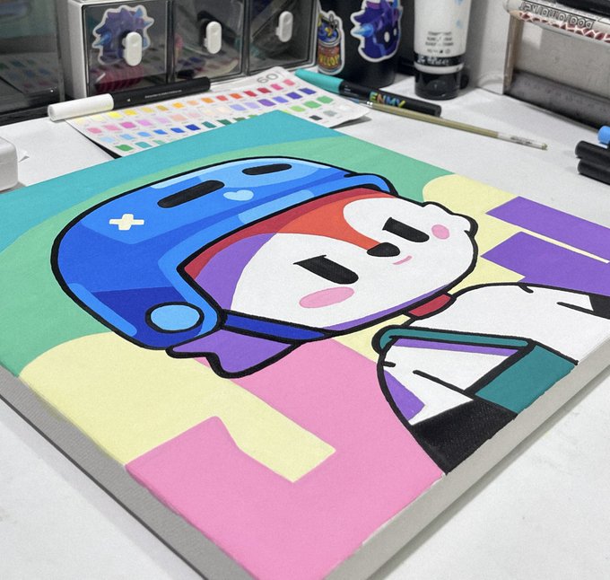 A vibrant marker and paint illustration on a canvas/sketchbook depicting a stylized character wearing a blue gaming-style helmet, surrounded by color swatches and art supplies on a desk.