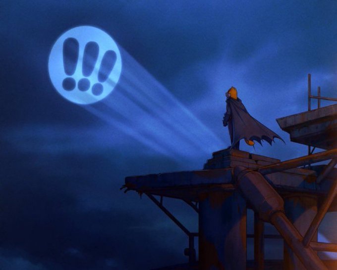 An animated scene of Batman standing on a rooftop at night, his cape billowing as the Bat-Signal shines into the cloudy sky above him.