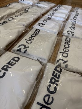 Multiple white plastic packages branded with the 'decredo' logo are stacked together in a warehouse setting.