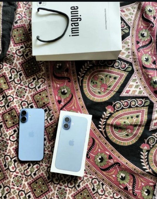 A blue iPhone is displayed alongside its white box on a paisley-patterned fabric, with a shopping bag reading "imagine." visible in the background. The image visually represents the post's message about a thoughtful gift, emphasizing that the genuine gesture behind the present matters more than its monetary value.