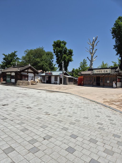 The image shows a brick walkway with buildings, including a small hut-like structure that appears to be an Asian restaurant or shop. The photo has been edited to include text from a post about a 70K party, which seems unrelated to the scene in front of it.