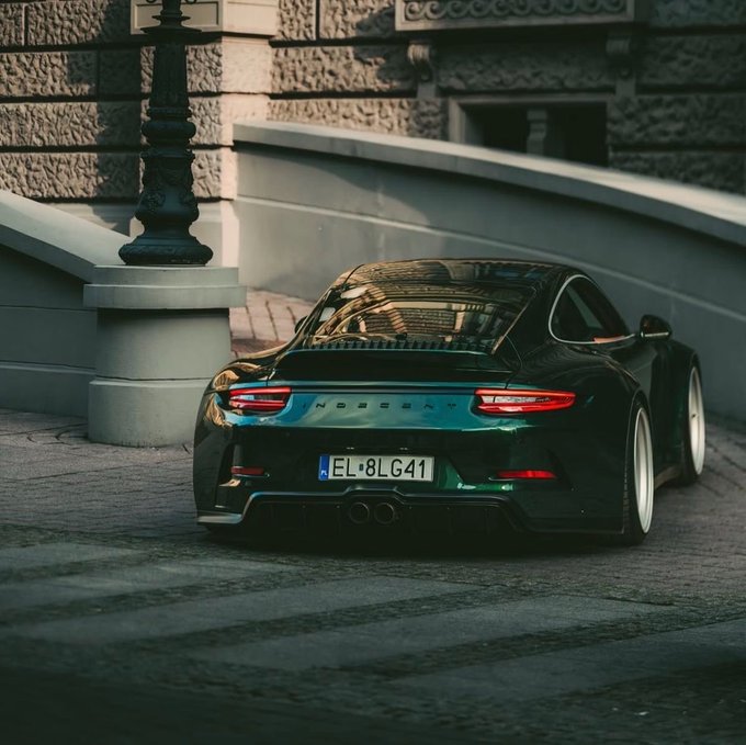 A dark green Porsche 911 with the license plate 'EL 8LG41' is parked on a cobblestone street near a stone building and lamppost.