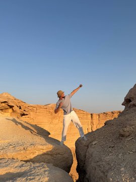 A man triumphantly leaps with arms raised across a rocky canyon gap, embodying the celebratory spirit of the post as he soars over the desert terrain like Bitcoin reaching new bullish heights.