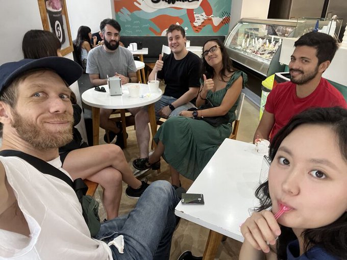 A group selfie of six people sitting around small tables in what appears to be an ice cream shop.