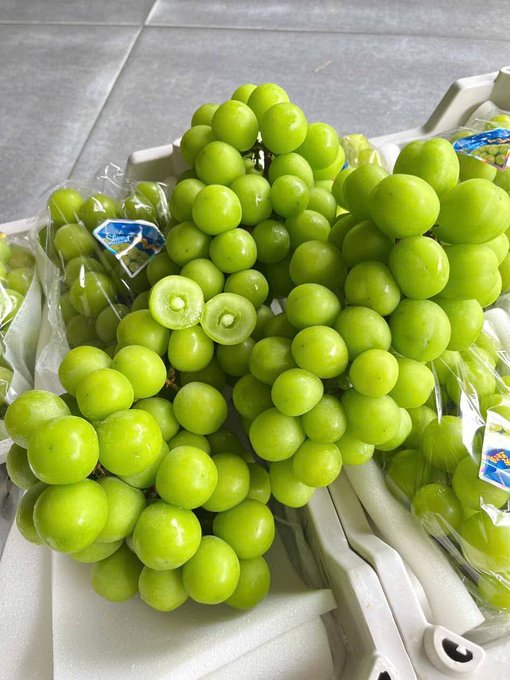 The image features a bunch of green grapes, possibly grapes or grapesauce, sitting on top of a table. The grapes are surrounded by plastic bags, which could be used for packaging or storage purposes. There is also an accompanying text that reads "Mới sáng bị đỏ tài khoản thì nên làm gì....mua nho xanh ăn cho nó xanh lại Nho xanh ương nhân xanh 100k/kg.". The focus of the image is on the grapes and their packaging, providing a clear view of both elements together.