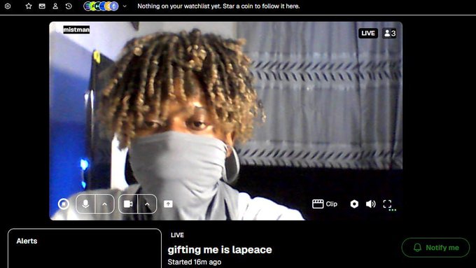 A livestream screenshot showing a person with curly hair wearing a light blue face covering, with the stream title 'gifting me is lapeace'.