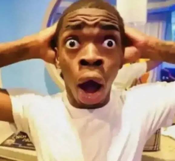 A young man with a surprised, wide-eyed expression holds his hands to his head in an exaggerated reaction shot.