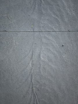 A close-up photo of a wrinkled gray fabric or sheet with a horizontal seam across the middle and some smudges or stains visible.