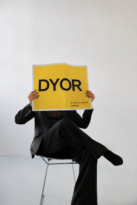 A person in a black suit sits on a chair, holding up a large yellow poster that reads "DYOR" (with smaller text "do your own research" and "binance" beneath it) in front of their face, reinforcing the GMWeekend theme of encouraging personal research and due diligence in the crypto space.