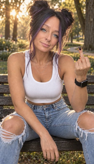 A young woman with dark hair featuring purple highlights sits on a wooden park bench, wearing a white crop top and ripped jeans while making a hand gesture.