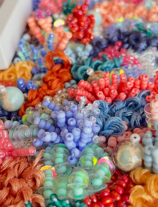 A vibrant, close-up display of colorful beaded jewelry and yarn crafts in shades of blue, red, orange, green, and gold.