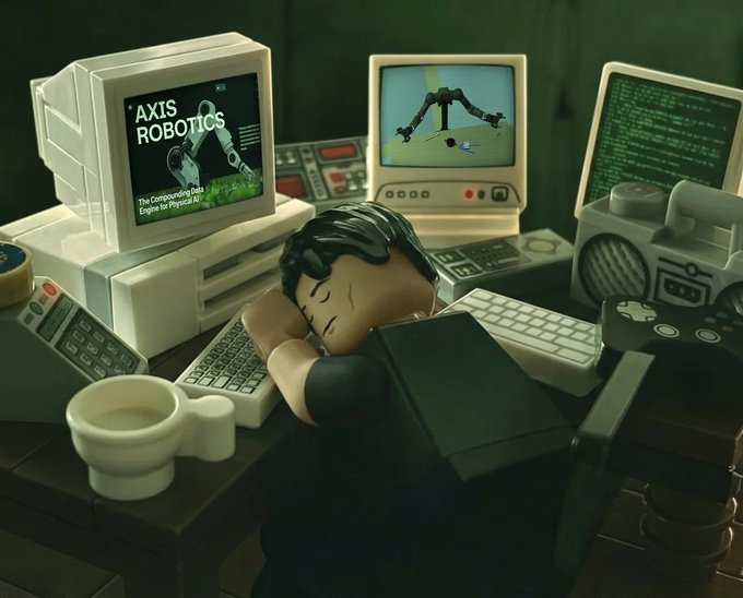 A LEGO figure rests his head on a desk surrounded by vintage computer monitors, one displaying 'AXIS ROBOTICS - The Compounding Data Engine for Physical AI' and another showing a 3D robotics simulation, with a coffee mug nearby.