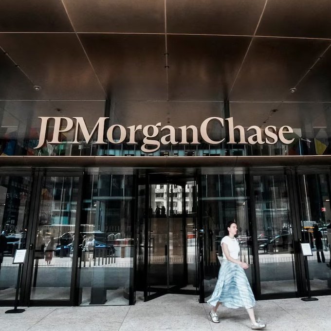 A woman walks past the entrance of a JPMorgan Chase bank branch, with the company's name prominently displayed in large gold letters above the revolving doors. The image visually underscores the article's news about JPMorgan severing its banking relationship with Polymarket, symbolizing the financial institution at the center of the regulatory dispute.