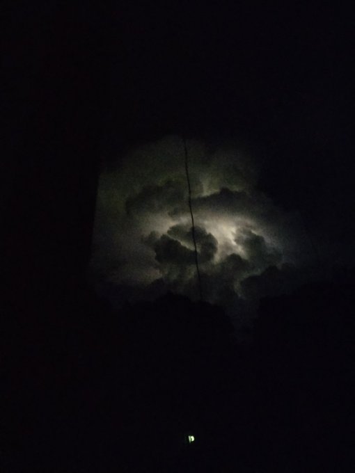 A nighttime view of the moon partially obscured by clouds, framed by dark silhouettes.