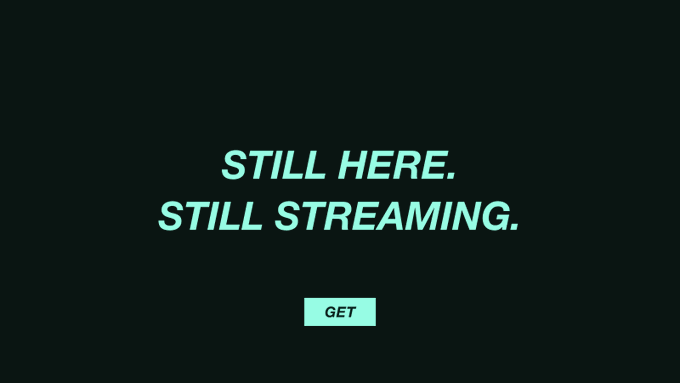 A minimalist black screen with light teal text reading 'STILL HERE. STILL STREAMING.' above a 'GET' button.