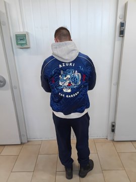 A person stands facing a door, showing off the back of their blue "AZUKI - THE GARDEN" graphic T-shirt, which aligns with the post about their love for the Azuki community and matching merchandise.