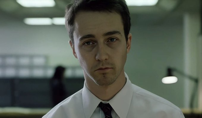 A close-up portrait shows actor Joseph Gordon-Levitt in a white dress shirt and tie, looking directly at the camera in a dimly lit office setting.