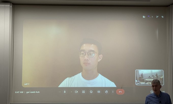 The image shows a man wearing glasses sitting at a desk, with a projector screen displaying an image of him smiling. The caption for the image reads "Jeff ( @chameleon_jeff ) beaming in to the NYU CBER conference today $HYPE @cryptoeconprof @NYUStern". This suggests that Jeff is attending a virtual event or conference and is sharing his happiness with others through the projector screen.