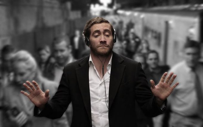 A black and white photo of a man in a suit and headphones with his eyes closed and a serene smile, holding his hands up in a crowd.
