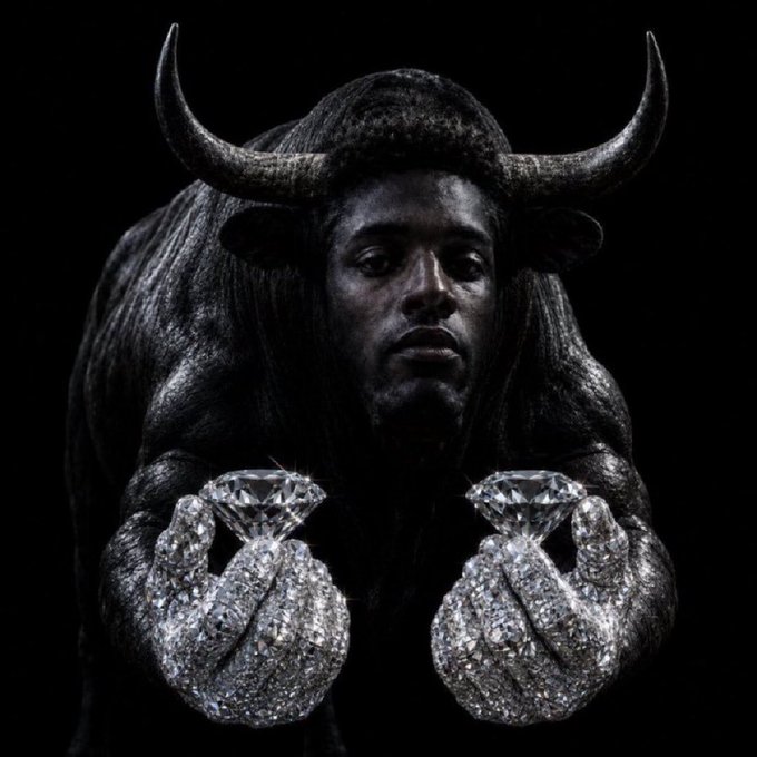 A dramatic dark image shows a figure with a bull's head and horns holding two large diamond-covered hands presenting diamonds against a black background.