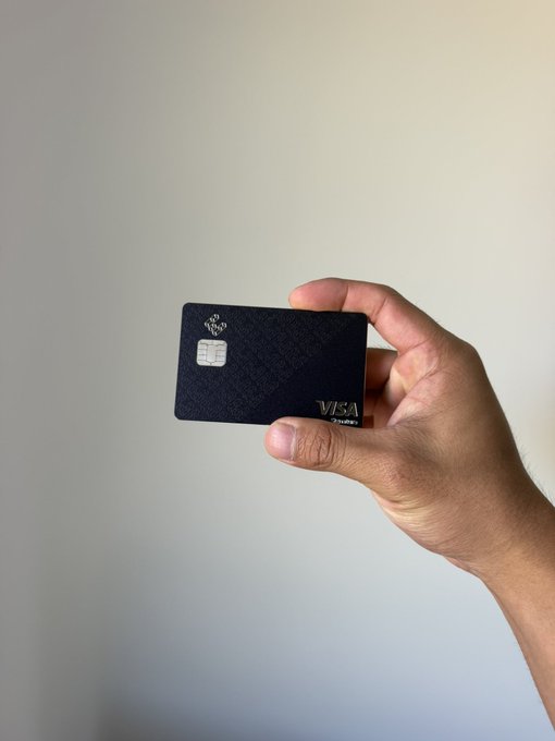 A hand holds a dark navy textured Visa credit card with a chip visible against a plain white background.