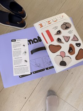 A new MATIC robot kit, including an instruction manual and a sheet of expressive sticker face decals, sits on a light blue box on a wooden floor near a pair of sneakers. The unboxing image accompanies the announcement of the new @maticrobots robot.