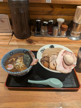 A tray of Japanese food including a bowl of noodles, a bowl of chashu ramen with sliced pork and an egg, served with a blue spoon on a wooden table.
