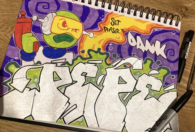 A hand-drawn graffiti-style illustration in a sketchbook showing a green alien-like character with the text 'Set Phaser to Dank'.