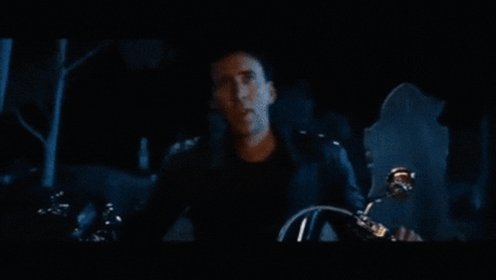 The image shows a man sitting inside a motorcycle with his hands on the handlebars. The background of the image is dark, which adds to the overall atmosphere of the scene. There are no texts or other objects visible in the image. The focus of the image seems to be on the man and the motorcycle, possibly indicating that he is about to embark on an adventure or ride through a dangerous area.