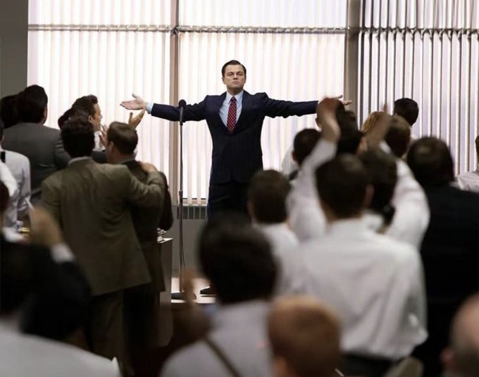 Leonardo DiCaprio in a scene from 'The Wolf of Wall Street' standing triumphantly with arms outstretched before an adoring crowd.