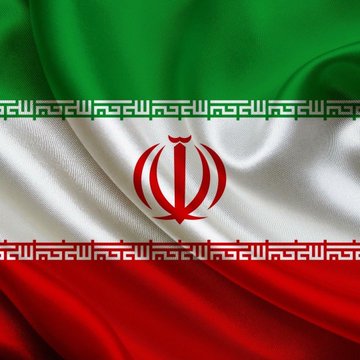 A close-up of the Iranian flag, featuring its horizontal green, white, and red stripes with the national emblem in red at the center and stylized Kufic script bordering the white band. The flag's prominent display complements the post's tone of recurring tension or conflict involving Iran.