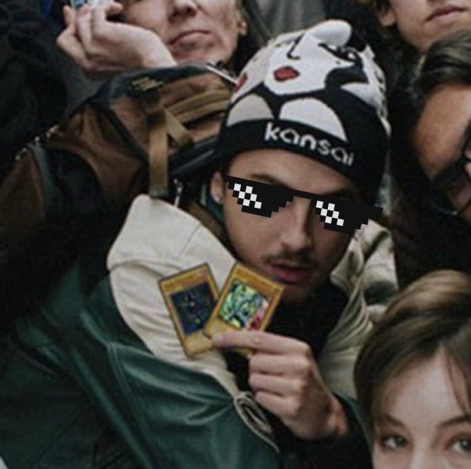A young man wearing pixelated "deal with it" sunglasses and a Kansai skull cap holds up two Yu-Gi-Oh! trading cards with a determined expression, surrounded by friends. The "gl to us" caption reflects the wishful optimism of opening card packs, hoping for a lucky pull in a game defined by chance.