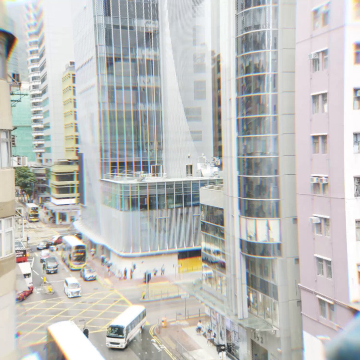The image shows an urban cityscape with tall buildings, buses, and pedestrians on the street below, viewed from above with a blurred, dreamy filter applied. The connection to the post appears ironic or contrasting—the calm, bustling city scene juxtaposed with a promotional caption for KODA plushies, possibly using the image to convey a sense of urban isolation or the desire for comfort objects amid city life.