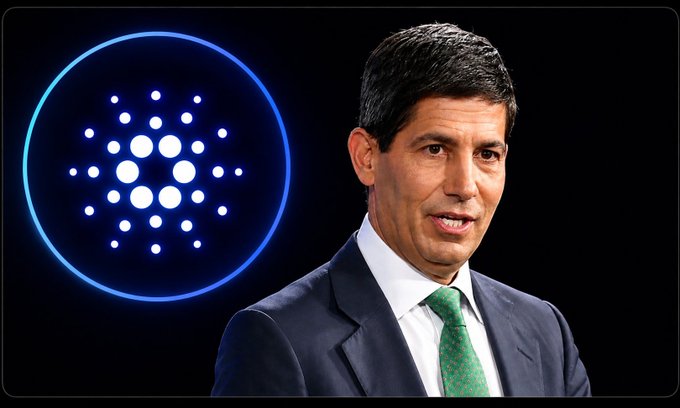 A man in a dark suit and green tie stands next to a glowing blue circular logo featuring a dot pattern, resembling the Cardano cryptocurrency emblem.