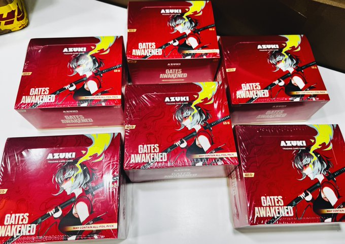Multiple "AZUKI GATES AWAKENED" booster boxes featuring anime-style character artwork are stacked together, corresponding to the Azuki Care Package mentioned in the post that was made possible with help from @RiceRiddler and @f10wer.