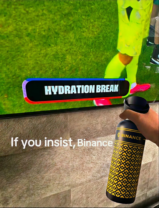 A hand holds a black and yellow Binance water bottle in front of a TV displaying a soccer match with a "HYDRATION BREAK" graphic, accompanied by the caption "If you insist, Binance" — playfully referencing a sponsored hydration break during the game.
