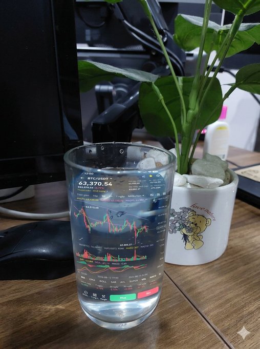 A glass tumbler displaying a BTC/USDT trading chart sits on a desk next to a potted plant in a "love nature" planter.