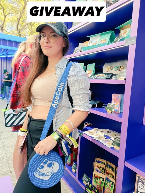 A woman wearing glasses and a cap poses in front of a blue and purple display shelf, with a 'GIVEAWAY' banner overlaid at the top of the image.