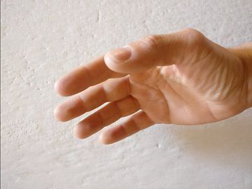 The image shows a close-up of a person's hand with their thumb extended outwards. The background appears to be a white wall or surface. There are no other objects or people visible in the image, making it a simple composition focused on the hand and its position relative to the viewer.