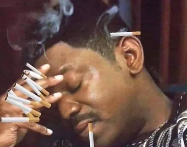 A man appearing to smoke multiple cigarettes simultaneously, with several cigarettes held between his fingers and others placed on his face, surrounded by smoke.