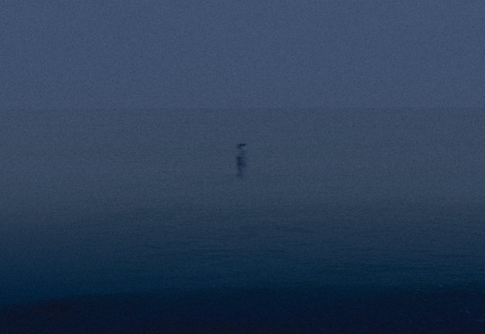 A hazy, dark blue image showing a small, indistinct object hovering over what appears to be a foggy body of water, with a grainy, low-light atmosphere and no visible text or numbers. The obscure, solitary subject mirrors the ethereal "Wandering Soul" theme of the post, though the listing's price of 0.00 ETH is not visible in the image itself.